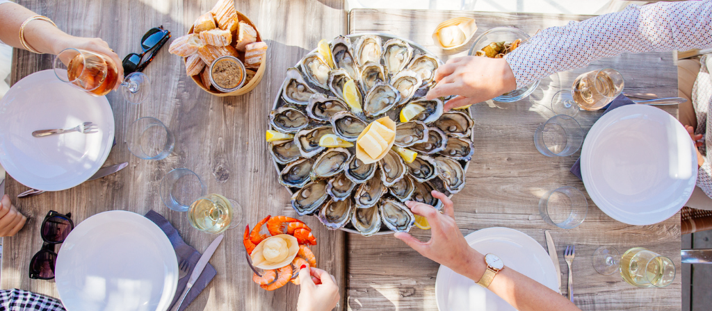 Table with a platter of oysters, prawns and glasses of wine
