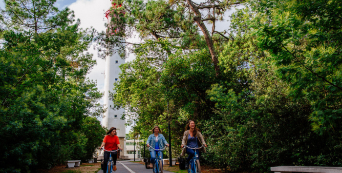 3 jeunes femmes à vélo devant le Phare du Cap Ferret