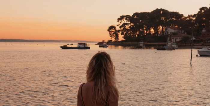 Jeune femme de dos regardant un coucher de soleil face au Mimbeau et à la Dune du Pilat